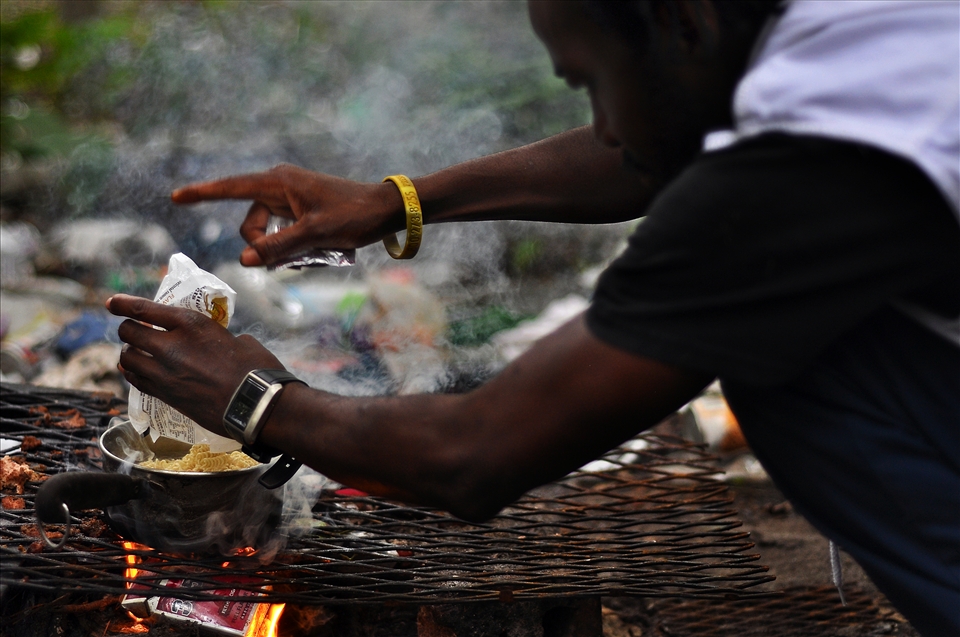 A resident of Tent City prepares a pot of noodles atop a pile of burning garbage
