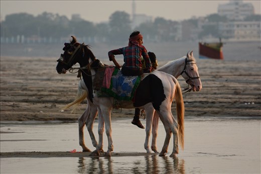 Boys take their horses out for a ride beside the river.