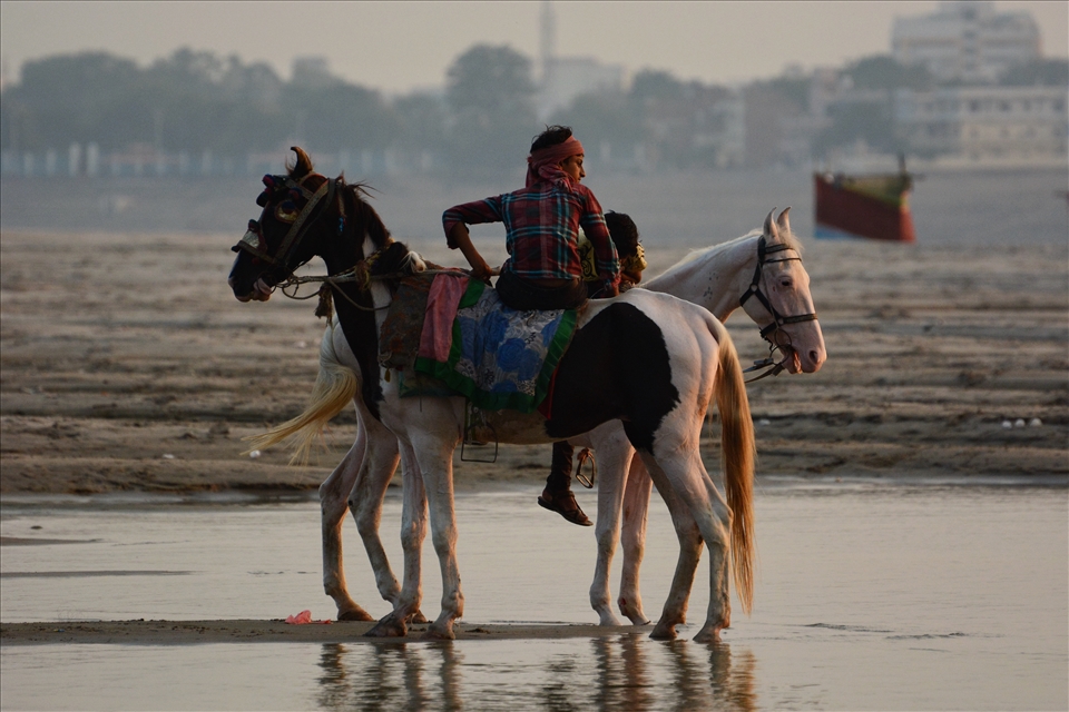 Boys take their horses out for a ride beside the river.