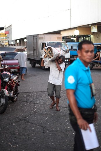 an elderly man carries a heavy bundle of lumber across the market