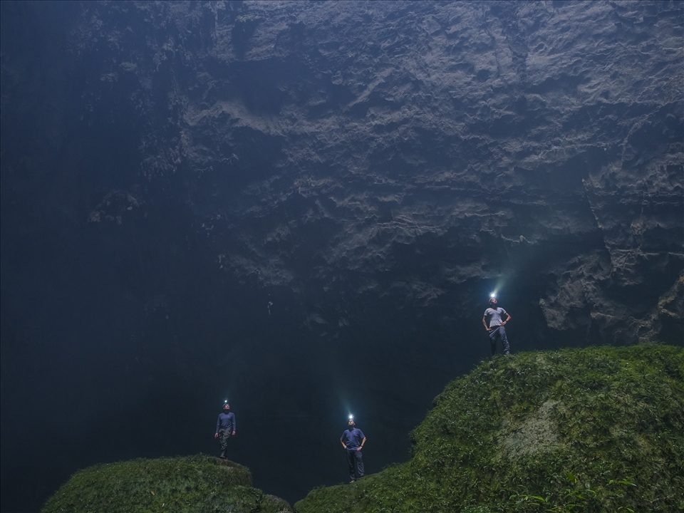 Expedition members try to light up the unbroken walls containing the doline. Water falling from the top of the doline form mist at this lower level in the cave.