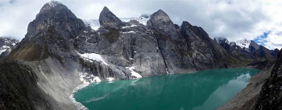 The pristine glacial lake Viconga is encroached upon by ominous storm clouds as they gust through the jagged peaks of the Andes - Cordillera Huayhuash, Peru