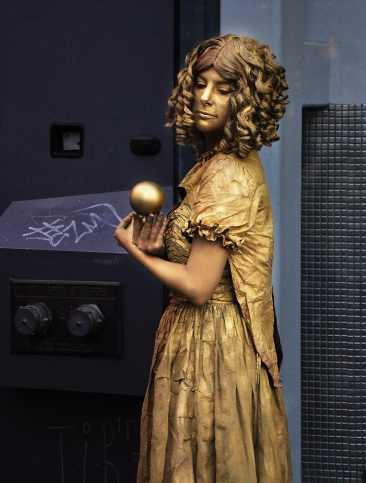 In the midst of busy Granville Street, twirling and manipulating a golden sphere, is a street performer named Dawn. Though she appears peaceful, this image was preceded by a series of twist and turns manipulating the sphere in such a way that it revolves around her body then alas,  the spiral ends. It is a micro-cosmic reflection of the wider world and the universe. An example of action and reaction, and that as the juggler controls the sphere, we can control our destiny. 