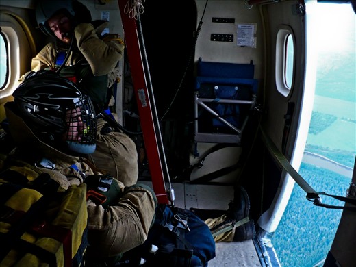 Two Smokejumpers, en-route to a fire, sit patiently and watch the world go by through the opening they will soon depart through.
The use of fixed-wing aircraft and parachutes allows for crews to be placed on fires in remote locations far more quickly than other methods; allowing for fires to be extinguished quickly and before they grow too rapidly.
