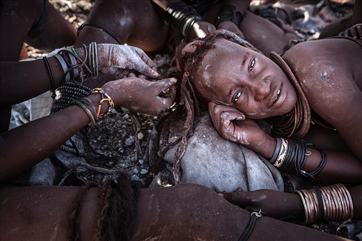 Once the daily chores are completed and the days temperature begins to soar, the women retreat back to the shade where their beauty salon continues. A Himba woman's hair is drawn into dreadlocks and encased in a thick ochre casing which adds to their beauty, but it is a laborious process that requires all hands to assist removing and replacing the delicate casing every 4 weeks or so.