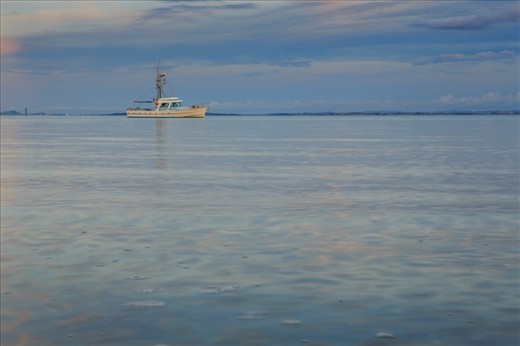 Was walking along the shore of Cornwallis  Beach New Zealand, during sunset and snap this boat alone in the sea and the sky makes a beautiful colour in the sea.