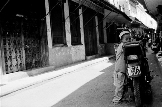 Latif clutches the seat of his father's motorcycle. He attends school every day, learning the basic principles of Islam, but  he knows that one day he will be a man like his father: a provider.