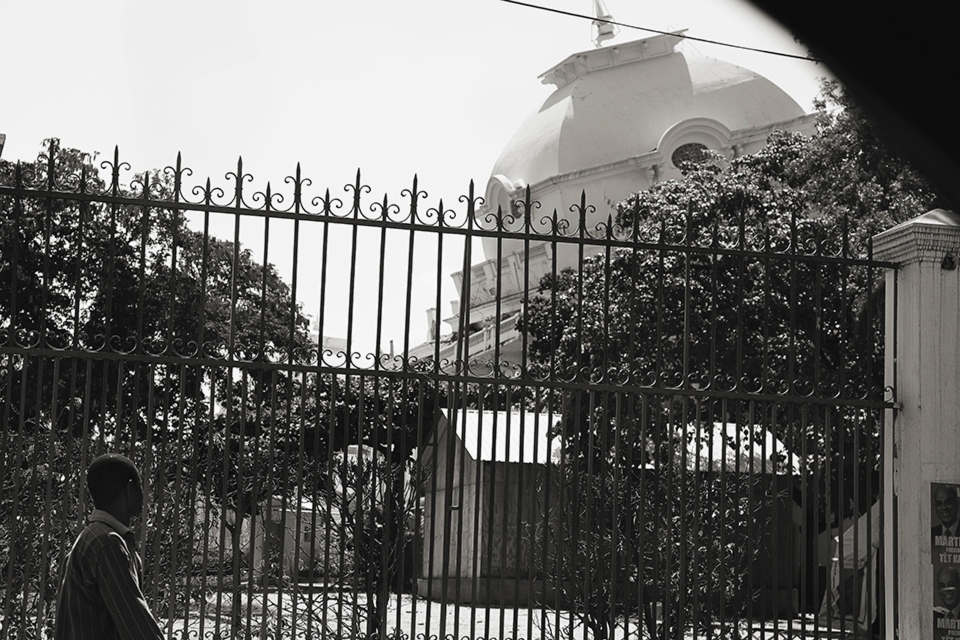 A Haitian man walks by the now leaning and heavily guarded Palais National.  For a year after the quake, government officials were still seen removing government materials out of the heavily damaged building.  