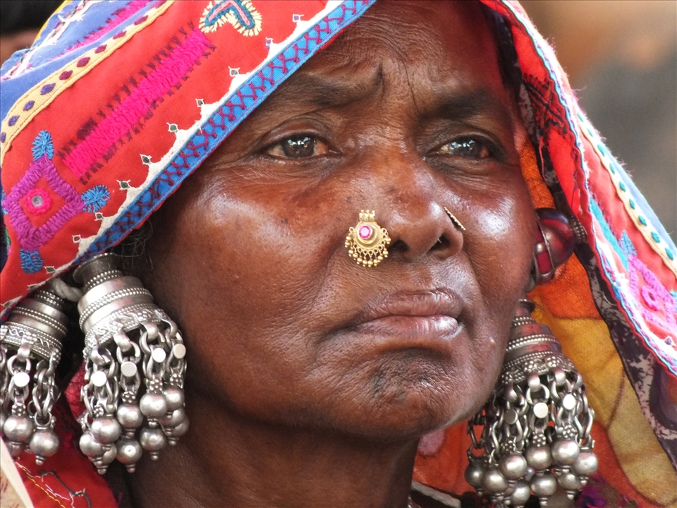 A weary woman from a remote village, in full tribal wear, listening for hope