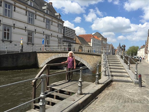 Brugge -- Cindy on wooden steps leading down to canal -- bridge in background