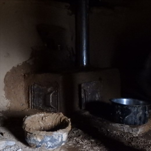 A stove (chulha) nearing completion. In the foreground is a pot full of 'lal mart' (red clay) used for rendering the unit.