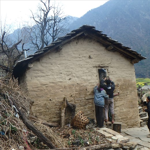 Daytime light is imperative in a Kumaoni house for cooking. UV stable thick plastic was used on the small windows. The effect is brilliant - you can cook without needing to switch on the solar light.Here is a shot of Dinesh and Hira organising plastic for the window (note the flue on left hand side of building).