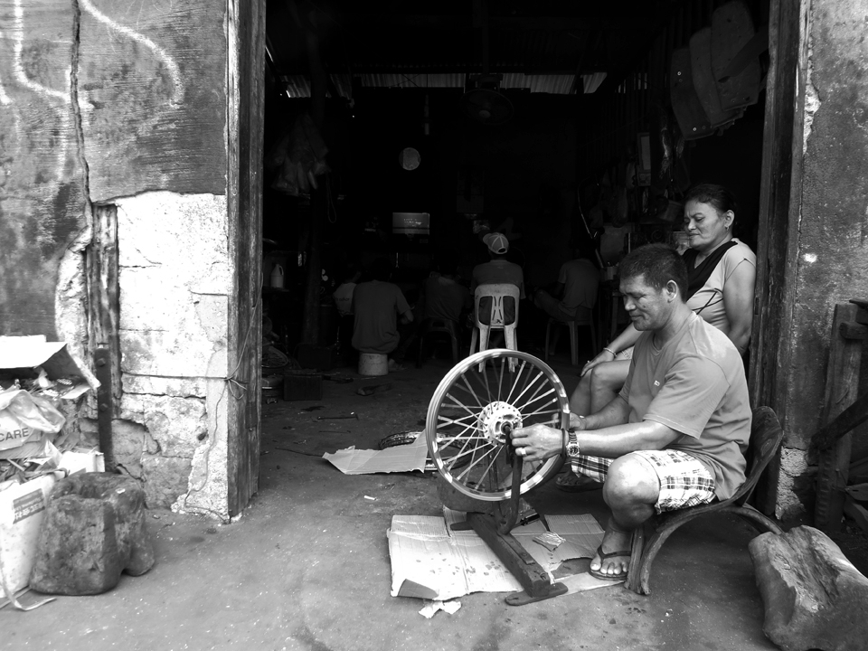 In a remote province in the Philippines where motorcycle is the common mode of transportation. This fixes a motorcycle rim while his colleagues watch TV on a slow day.