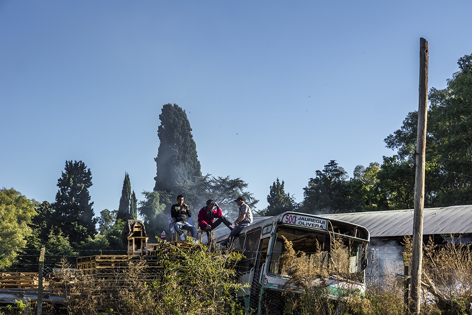 Neighbors from a near junkyard gather over an old bus to watch the rodeo.