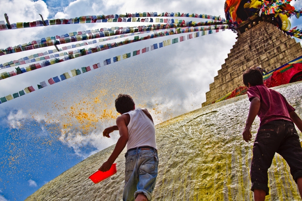 Whitewashing the Bouddhanath stupa is an ancient ritual aiming for conservation while at the same time is a symbol of renovation and continuity. Twice each month the painters repaint the stupa by pouring the white color on all over the dome then adding yellow color arcs round the stupa in the shape of a double lotus flower. In this picture two men are pouring the yellow color skillfully to make arcs in the shape a lotus flower.
