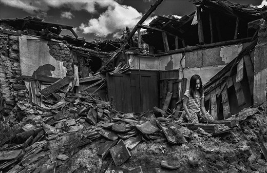 Girl lights a candle at the ruins of her grand parent's house 