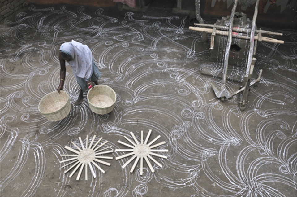 An old lady places buskets on earthern floor decorated with hand made designs 