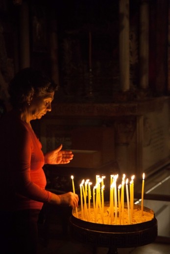 An older woman lighting candles in the near darkness of The Church of the Holy Sepulchre a few steps from the Golgotha altar, despite a crush of people from around the world, the woman had the space to herself and a moment of silence.