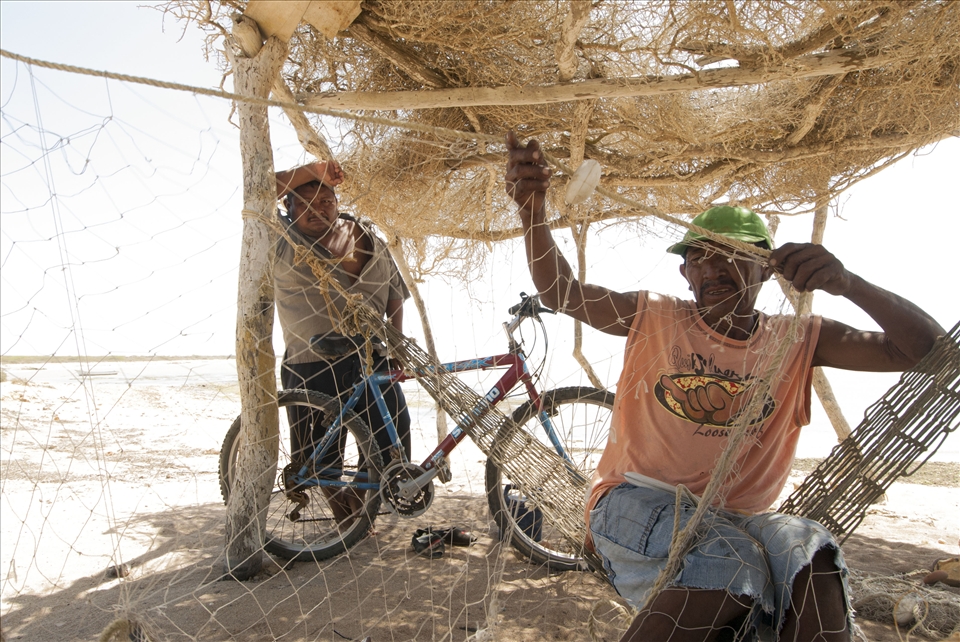 Sheltered from the noon sun, Pedro fixes the new holes in his fishing net 