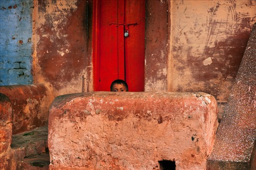 A boy hides whilst checking out the westerners walking down the street.