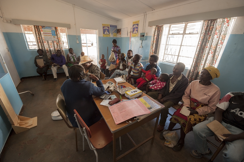 A woman prepares to have her blood pressure taken while others sit and wait. Some patients walk more than 20km in search of aid.