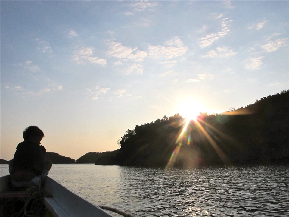 The sun rising on our right while the boy in front directs the boat to safety.
