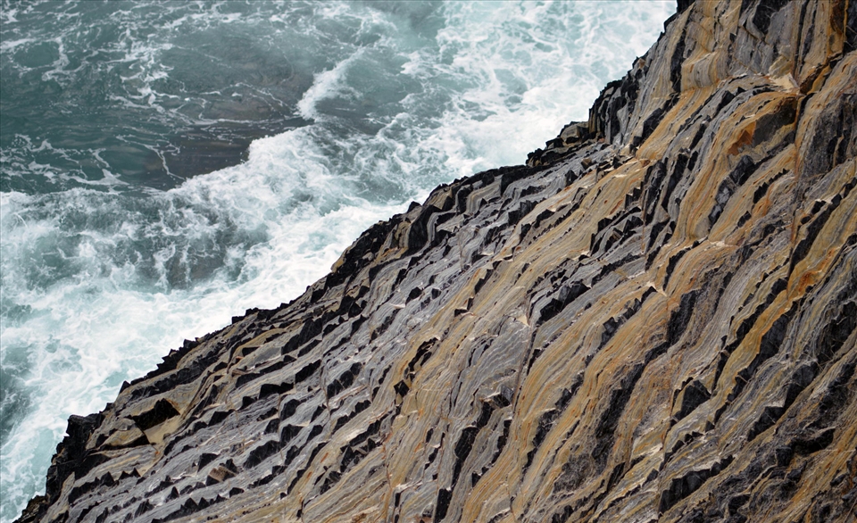 The Pacific Ocean crashes against a rigid cliff face of the Australia coastline.