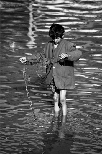 At the Pashupati Hindu Temple in Kathmandu, this young street boy, armed with a rope and magnet, fishes for coins (used as funeral offerings) in the holy waters of the Baghmati River, amongst the cremated remains of corpses. 