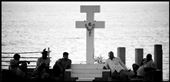 A cross stands tall against the mighty ocean as the locals chill around it.: by capturerapture, Views[204]