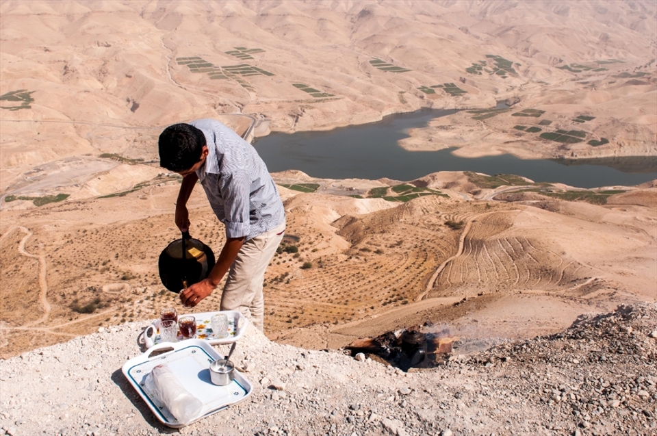 A boy serve some tea to the tourist. He made a fire along the cliff of the canyon