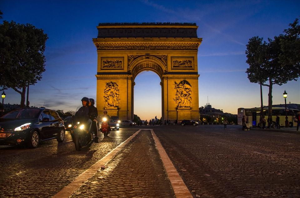Sun Sets behind the Arc de Triumph and traffics buzzes on the Champs Elysees. 