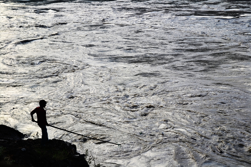 A solitary figure, fishing for driftwood, silhouettes against the swelling Ganges.
During Monsoon season, India's main 'Giver of Life'', the Ganges River, swells considerably, creating a bigger hazard to those who risk their lives collecting driftwood to make furniture and other marketable produce.
