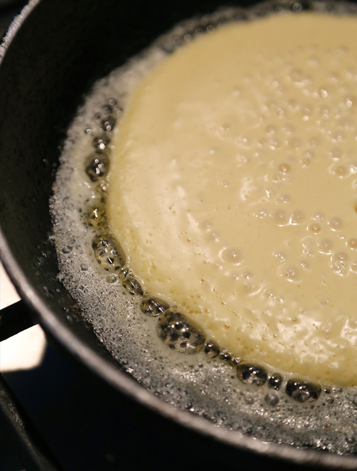 The pancake cooking in pan and ready to flip.