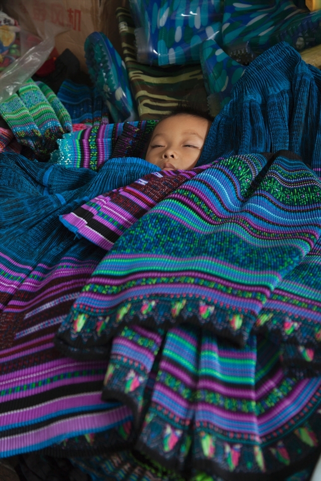 Fluttering his eyelids in a peaceful sleep, this cherished baby has been carefully placed amongst it’s mothers produce whilst she sells traditional hand made cloth at a local market in the remote hills of Sapa.
