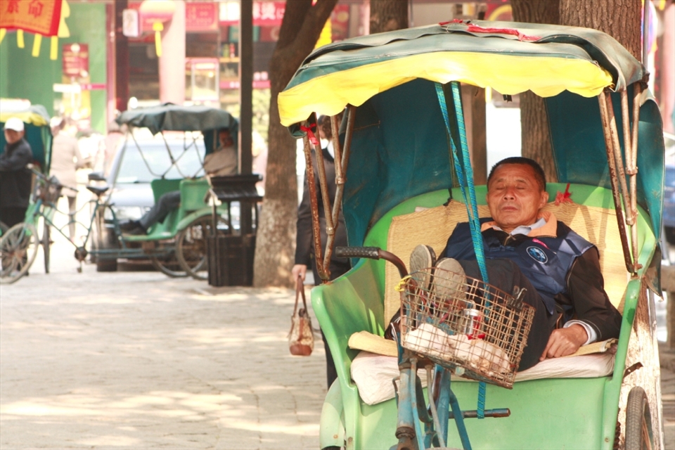 The value of a nap.     
This taxi man takes a late morning rest after a seemingly quiet morning. He might miss his only chance at business that day as other taxis wait in the background. 
