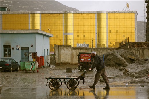 A man pushes a cart in the rain past one of Kabul’s many wedding halls. 

The wedding halls are the largest buildings in the city, typically gaudy in design and lit up with colourful neon lights at night. They are a stark contrast to the general poverty of the surrounds and the grey of the dust-coated city. 
