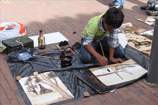 In Bogotá a boy strokes the final touches to his painting in hopes of a buyer.