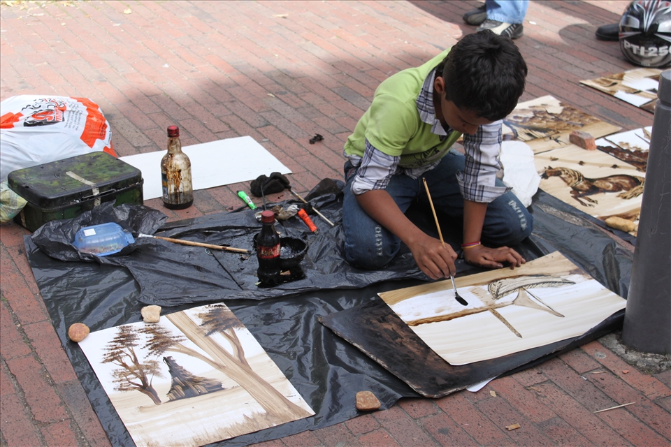 In Bogotá a boy strokes the final touches to his painting in hopes of a buyer.