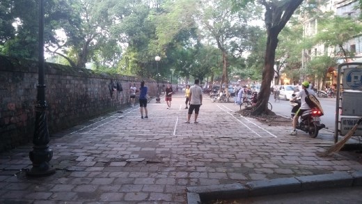 Playing badmington in the evening in the park is a popular activity. Here they've marked the court on the sidewalk. Must be parking is not allowed here.