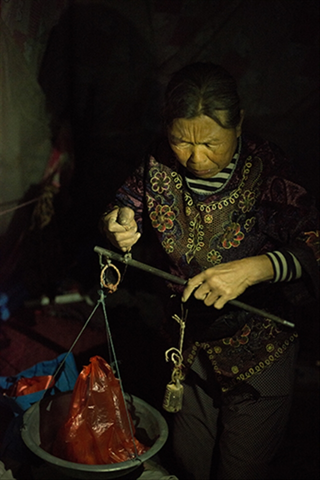 An elderly woman takes time out of closing her fruit stall to weigh apples with an old fashioned form of scales. 
