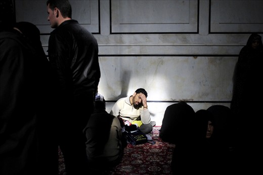 A man is sitting down among other Shiite pilgrims in the Shrine of Hussein chamber. Umayyad Mosque, Damascus, Syria.