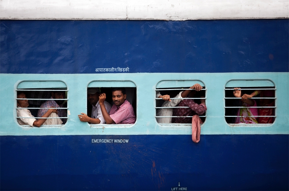 An overcrowded train transports workers, and those looking for work, from town to town. In the middle of the Indian summer, with temperatures exceeding 40°C (104°F), the conditions within those 3rd class, non air conditioned carriages are sweltering. Yet day after day, these trains are full to over-flowing. 