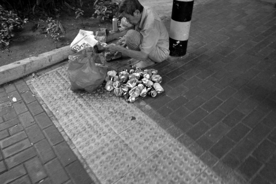 With a brick in one hand, he pounds on the drink cans to flatten them so he can squeeze more into a single bag for easier transport. Noise fill the surrounding as concrete meet metal incessantly but the crowd pass by almost oblivious to the ruckus. In a country touted to have the most number of millionaires per capita in the world, not everyone is living the high life.