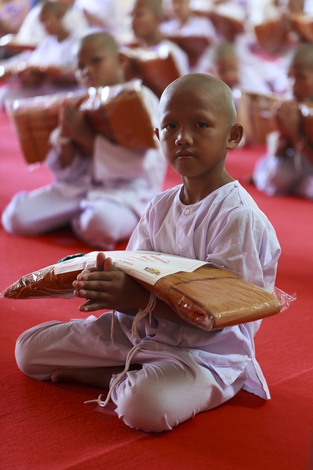 2) Inside, the temple is filled with monks, dignitaries and the family members of the 65 boys that are commencing with the ordination ceremony to become novice monks. The boys wear white robes for the days prior to their ordination, where they learnt of the rigors of their future life and that represent Brahmanism, the religion before Buddha’s enlightenment. With newly shaven heads and white strings about the wrists for good luck, they kneel holding their new robes.
