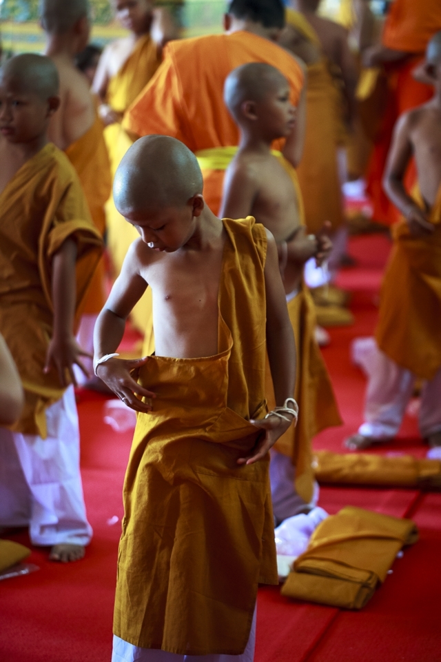 3) After taking their vows, this young boy tepidly examines his new garments. The monks help each boy to dress in their new saffron coloured robes, which signify their new life’s path.
