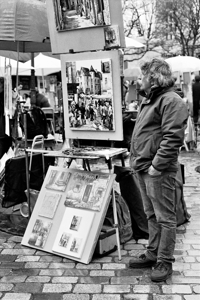 A man stands beside his artwork at Place du Tertre. He is one of the many artists who flock to Montmartre's most popular square in order to sell homemade masterpieces to passing tourists.
