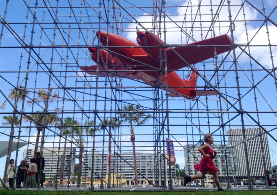 (3) This image of a young girl running past the work “Stasis’ by Claire Healy and Sean Cordeiro outside the front of the Museum of Contemporary Art in Sydney, looks at the idea of active participation in public art.  We can without knowing, be creating art, while observing it. With the plane heading off to the left and the girl running off to the viewers right, I was lucky that her bright pink dress helped to tie the two elements together. 
(This photo was taken with an iPhone)
