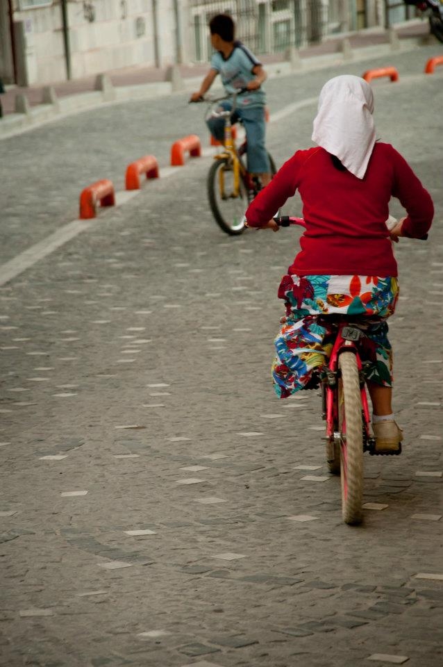 A girl riding a bike on the street of a residential place with her friend.