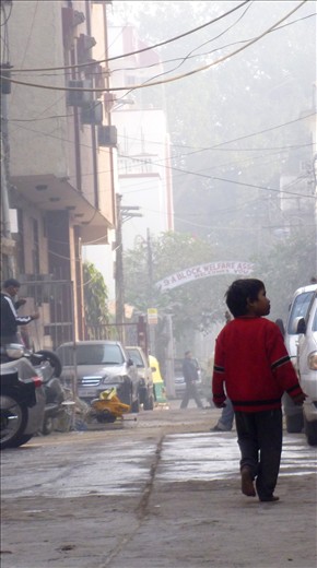 A lone boy walking bare foot down a quiet back street of New Delhi.