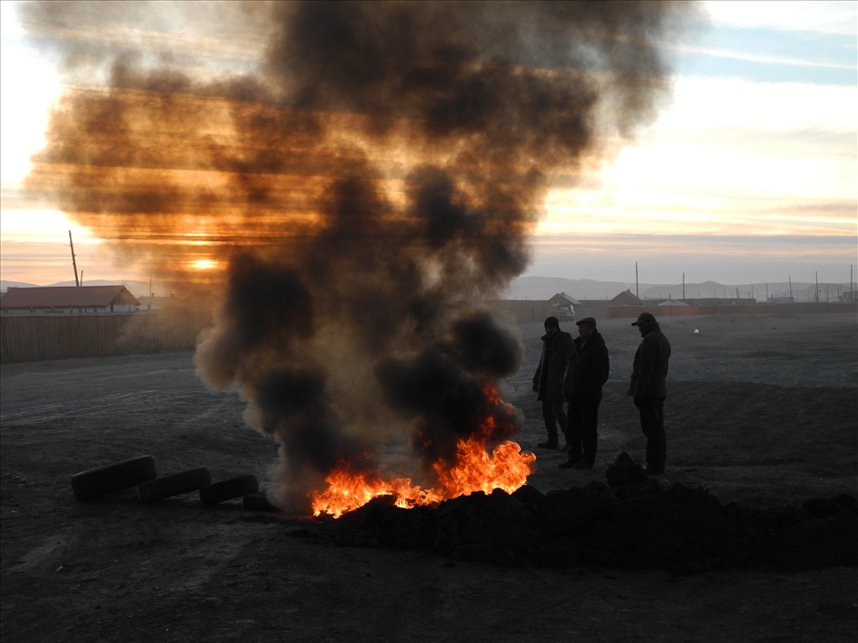 Builders burn tires in the street to defrost the ground for digging work. Zuunkharaa, Mongolia
